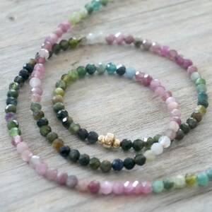 May include: Two multi-colored gemstone beaded necklaces with a gold clasp. The necklaces are made of pink, green, and blue gemstones.