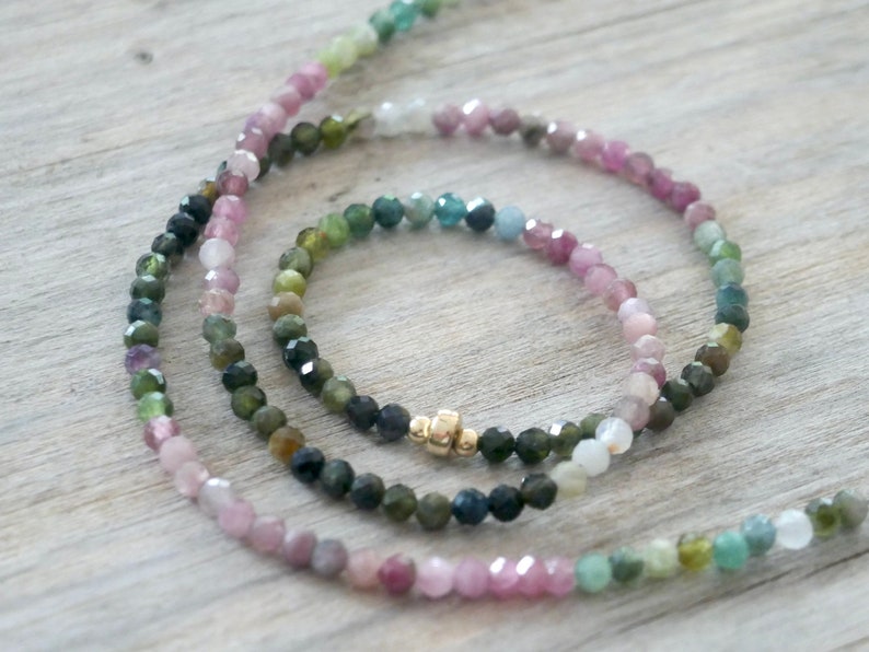 May include: Two multi-colored gemstone beaded necklaces with a gold clasp. The necklaces are made of pink, green, and blue gemstones.