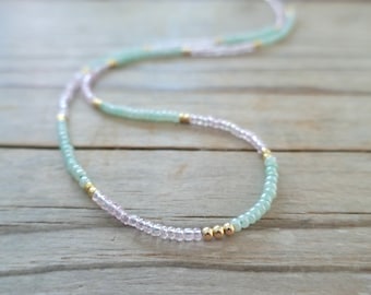 May include: A delicate necklace made with tiny light green and pink beads interspersed with gold beads.