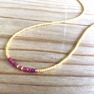 May include: A delicate gold chain necklace with a single row of small, deep red beads.