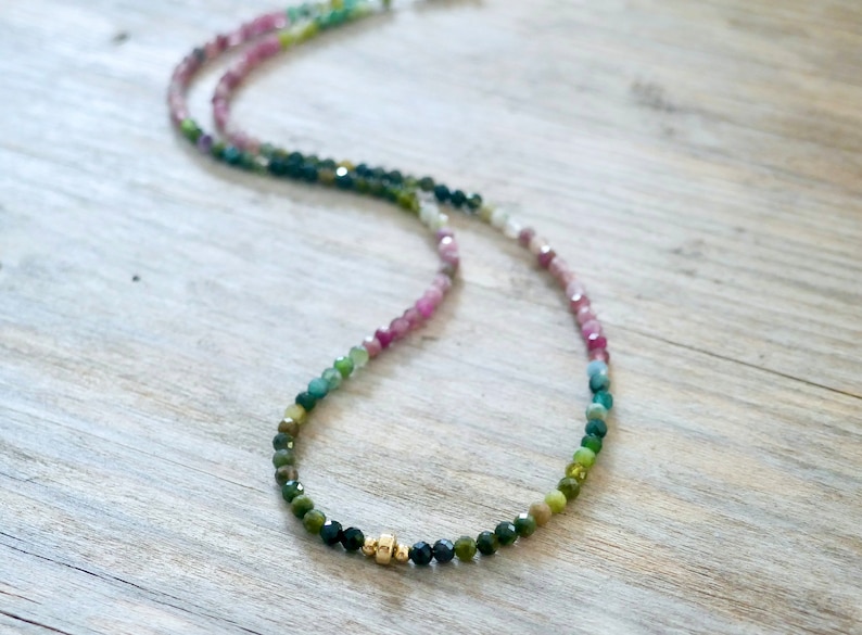 May include: A multi-colored gemstone necklace with a gradient of pink, green, and blue beads. The necklace has a gold accent in the center.