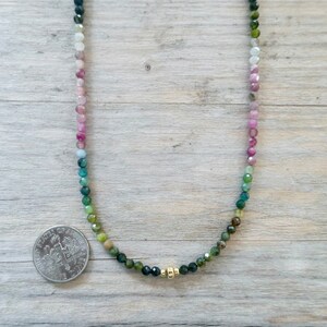 May include: A multi-colored gemstone necklace with a gradient of pink, blue, and green beads. The necklace is made with small, round beads and has a gold clasp.