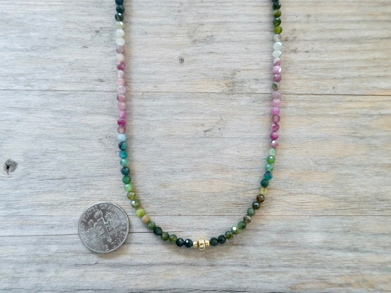 May include: A multi-colored gemstone necklace with a gradient of pink, blue, and green beads. The necklace is made with small, round beads and has a gold clasp.