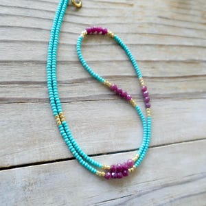 May include: A turquoise and gold beaded necklace with a cluster of pink beads in the center.