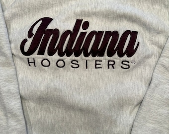 Może przedstawiać: Szara bluza z haftowanym logo w kolorze bordowym, na którym widnieje napis "Indiana Hoosiers" z symbolem znaku towarowego.