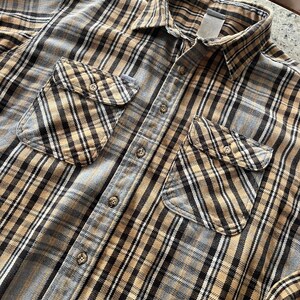 Pode incluir: Uma camisa de flanela xadrez marrom e cinza com fecho de botões e dois bolsos no peito.