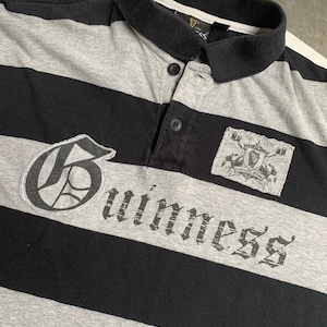 May include: A black and gray striped polo shirt with a large "Guinness" logo in a gothic font. The shirt also features a small patch with the Guinness logo and the text "Est. 1778" above it.