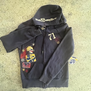 May include: A dark gray zip-up hoodie featuring the text Walt Disney World on the hood, the number 71 on the chest, and various colorful patches including a Mickey Mouse graphic. The garment includes long sleeves, a hood with drawstrings, and pockets.