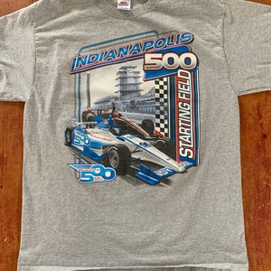 Puede incluir: Camiseta gris con un gráfico de un coche de carreras en una pista. El gráfico incluye el texto "Indianapolis 500 Starting Field".