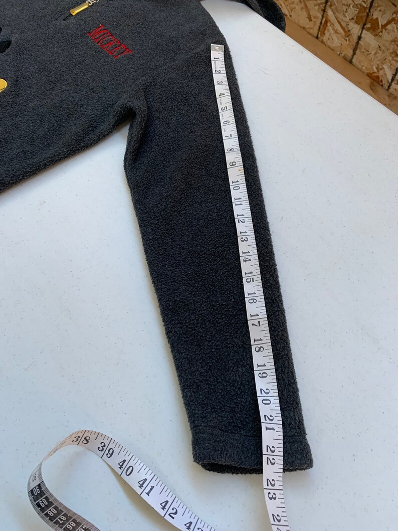 May include: Gray fleece zip-up jacket with a Mickey Mouse graphic and the word "Mickey" embroidered on the front. The jacket has a zipper closure and a stand-up collar. The sleeve length is 18 inches.