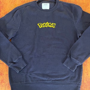 May include: A navy blue sweatshirt with a yellow embroidered "Pokémon" logo.
