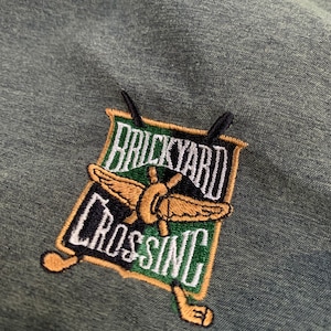 May include: An embroidered patch in green, black and gold with the text "Backyard Crossing" and a stylised butterfly design.