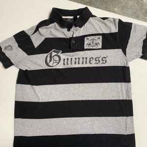 May include: A black and gray striped polo shirt with the word "Guinness" printed on the front. The shirt has a small patch with a crest on the right side of the chest.