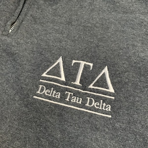 May include: A dark gray sweatshirt with a white embroidered Delta Tau Delta logo. The logo features the Greek letters "ΔΤΔ" and the words "Delta Tau Delta" underneath.
