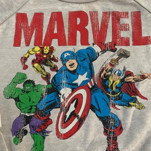 Puede incluir: Sudadera gris con un estampado desgastado del logotipo de Marvel y un grupo de superhéroes que incluyen al Capitán América, Hulk, Iron Man y Thor.