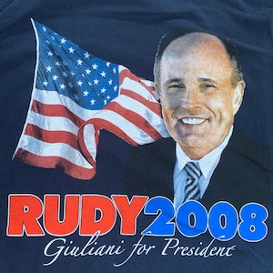 Könnte beinhalten: Ein marineblaues T-Shirt mit einer rot-weiß-blauen amerikanischen Flagge und einem Foto von Rudy Giuliani. Der Text "Rudy 2008 Giuliani for President" ist auf dem T-Shirt aufgedruckt.