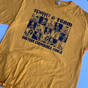 May include: A yellow t-shirt with a blue graphic of a basketball team. The graphic says "Indiana's D Team Eastern Conference Finals" and features a grid of 16 cartoon portraits of basketball players.