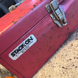 May include: A red metal toolbox with a silver latch and a white sticker that reads "STACK ON 16" All-Purpose Hip Roof Box No. R-516"