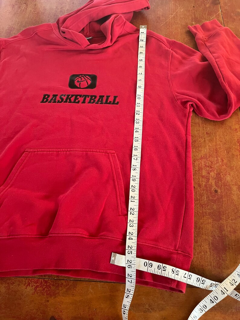 May include: Red hooded sweatshirt with a black basketball graphic and the word "BASKETBALL" in black lettering. The sweatshirt is measured with a tape measure.