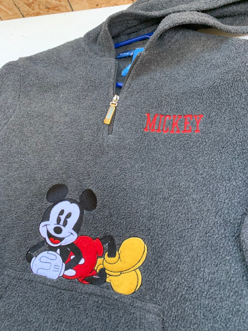May include: Gray fleece zip-up hoodie with a Mickey Mouse graphic and the word "MICKEY" embroidered in red.