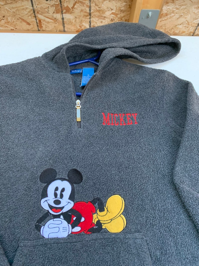May include: A gray fleece pullover hoodie with a red embroidered Mickey Mouse design and the word "MICKEY" in red embroidery.