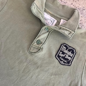 May include: A green long-sleeve shirt with a button-up collar and a patch that says "Makaha Surf Shop Hawaii". The shirt has a Hollister Co. label.