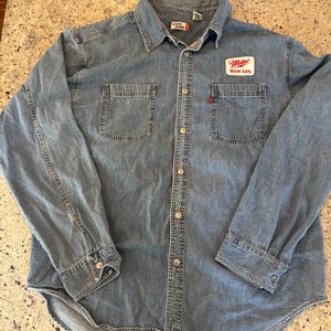 Może przedstawiać: Biały ceramiczny kubek z czarnym uchwytem i napisem "But First, Coffee" czarną, pogrubioną czcionką. Kubek stoi na białej powierzchni.