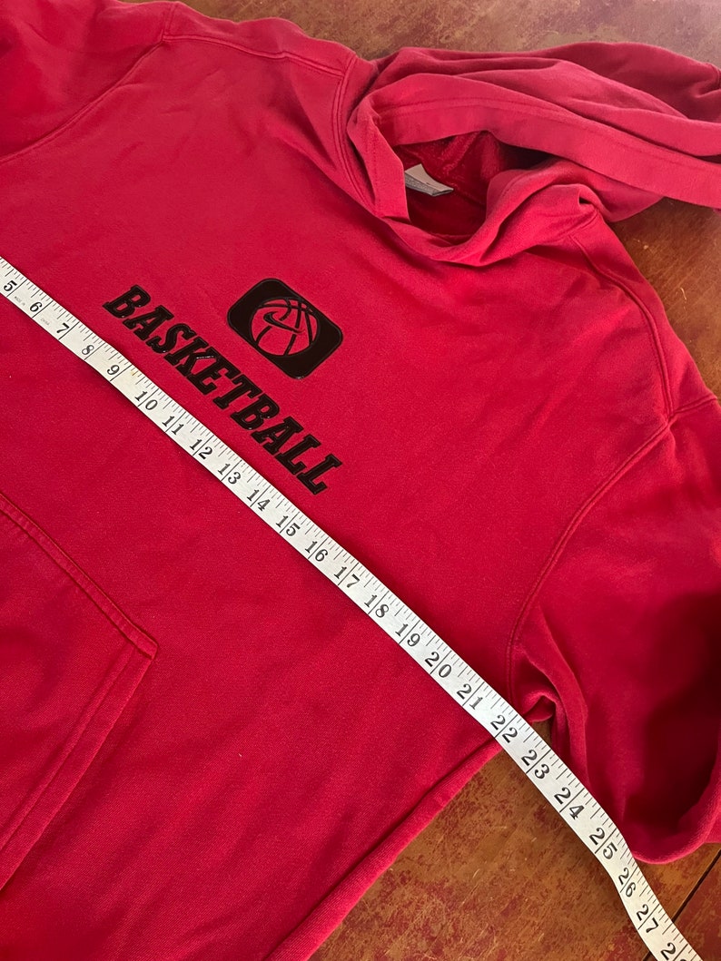 May include: Red hooded sweatshirt with a black basketball graphic and the word "BASKETBALL" printed on the front. The sweatshirt is measured with a tape measure.
