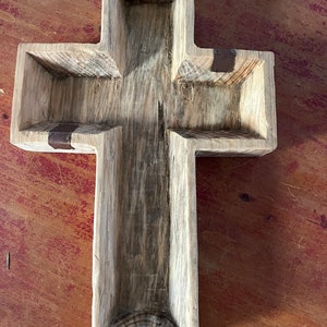 Könnte beinhalten: Ein Holzkreuz mit rustikalem Finish und vier Fächern. Das Kreuz ist aus hellbraunem Holz mit einer verwitterten Optik. Die Fächer sind mit Metallakzenten ausgekleidet.