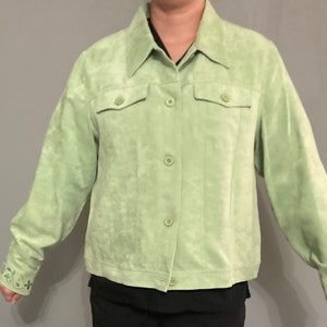 May include: A light green suede jacket with a button-up front and long sleeves. The jacket has two pockets on the chest and embroidered floral details on the cuffs.