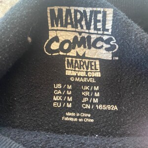 Puede incluir: Etiqueta negra con texto blanco que dice "MARVEL COMICS" y "MARVEL marvel.com" con un s&iacute;mbolo de copyright y un s&iacute;mbolo de marca registrada. La etiqueta tambi&eacute;n incluye informaci&oacute;n de tama&ntilde;o para EE. UU., Reino Unido, Canad&aacute;, Corea del Sur, M&eacute;xico, Jap&oacute;n y China.