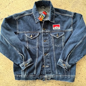 Puede incluir: Chaqueta vaquera azul con un diseño clásico. Cuenta con un parche de Marlboro rojo y blanco en el pecho y una etiqueta en el cuello. La chaqueta tiene cierres de botón, dos bolsillos en el pecho y dos bolsillos laterales.