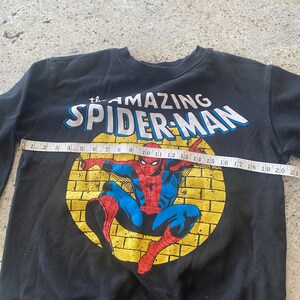 Puede incluir: Sudadera negra con un gr&aacute;fico de Spider-Man amarillo y rojo. El gr&aacute;fico dice "The Amazing Spider-Man".