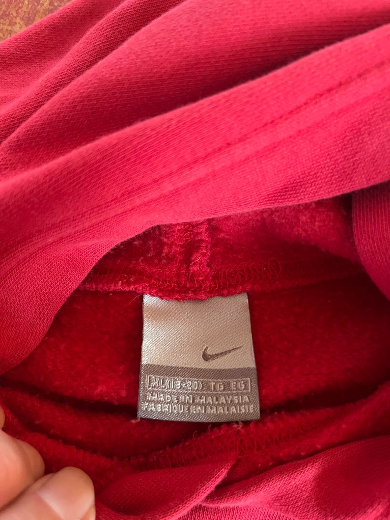 May include: A red Nike hoodie with a white tag that reads "XL (43-45) TG EG" and "MADE IN MALAYSIA FABRIQUE EN MALAISIE".