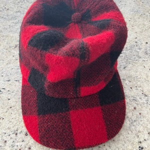 Pode incluir: Um boné de lã vermelho e preto xadrez com uma coroa arredondada e uma aba plana.