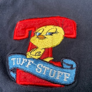 May include: A red and blue embroidered patch featuring a yellow cartoon bird with the text "Tuff Stuff" on a blue banner.