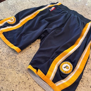 May include: Blue basketball shorts with yellow and white stripes. The shorts feature a logo on the right leg that says "Indiana Pacers".