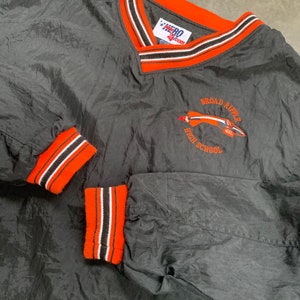 May include: Black windbreaker jacket with orange and white stripes on the collar and cuffs. The jacket has a v-neck and a logo embroidered on the front that says "Broad Ripple High School".