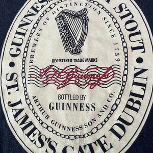 Puede incluir: Una etiqueta de cerveza Guinness Extra Stout de estilo vintage con un logotipo de arpa en blanco y negro, el texto "Brewers of Distinction Since 1759" y las palabras "St. James's Gate Dublin" en un dise&ntilde;o circular.