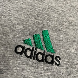 May include: A gray sweatshirt with a black embroidered Adidas logo. The logo features three green stripes.