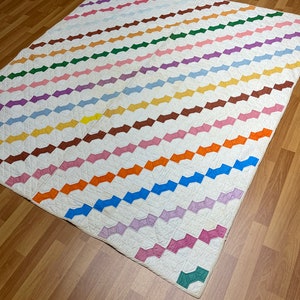 May include: A white quilt with a pattern of colorful bow ties. The quilt is made of cotton fabric and is quilted with a diamond pattern. The quilt is in good condition and has no visible stains or tears.