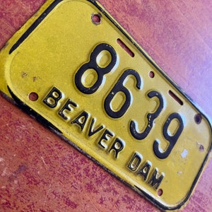 May include: A yellow metal license plate with black lettering. The plate reads "8639 Beaver Dam".