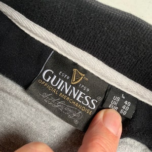 May include: A black and white label with the text "GUINNESS ESTD 1759 OFFICIAL MERCHANDISE" and a harp logo. The label also has the text "US L 40 UK 40 EUR 50".