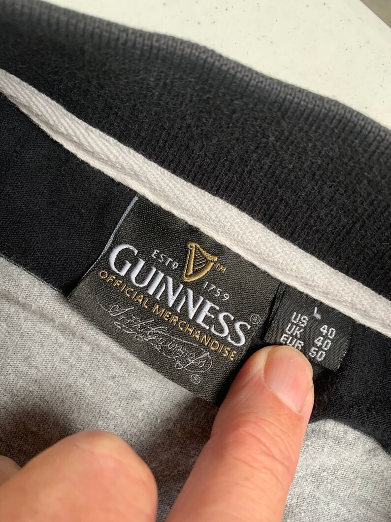 May include: A black and white label with the text "GUINNESS ESTD 1759 OFFICIAL MERCHANDISE" and a harp logo. The label also has the text "US L 40 UK 40 EUR 50".