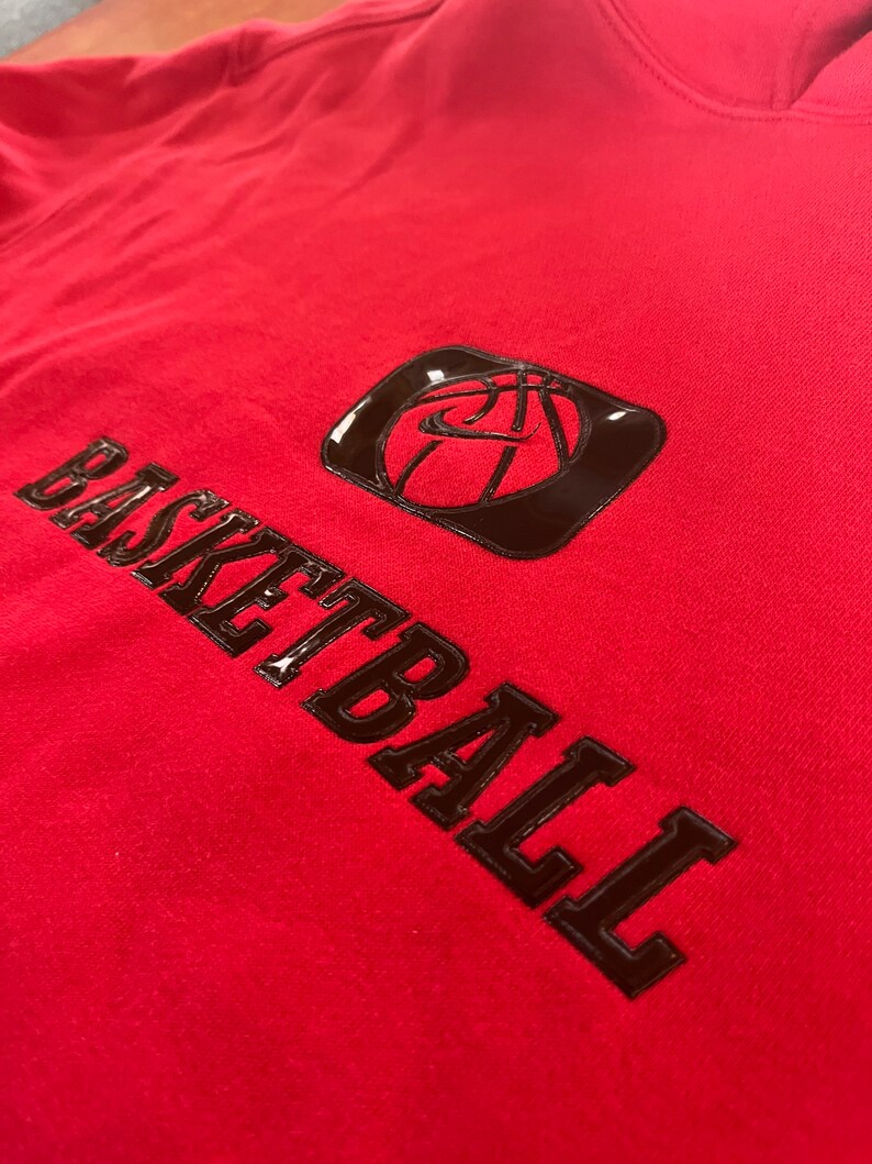 May include: Red hoodie with a black basketball graphic and the word "BASKETBALL" in large, bold, black letters.