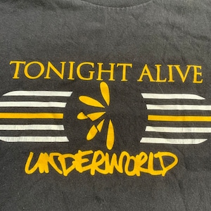 Op de afbeelding: Zwart T-shirt met een geel grafisch ontwerp met de tekst "Tonight Alive Underworld".