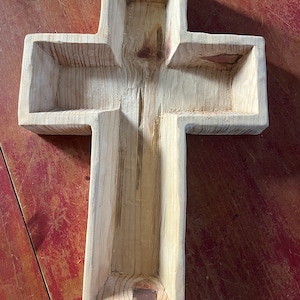 Könnte beinhalten: Ein Holz-Pflanztopf in Kreuzform mit zwei Metall-Akzenten oben und unten. Der Topf ist aus hellem Holz gefertigt und hat ein rustikales Aussehen.