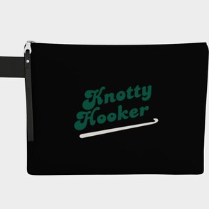 May include: Black zippered pouch with the text "Knotty Hooker" in green script, and a white crochet hook graphic. The pouch has a black handle and a silver zipper.