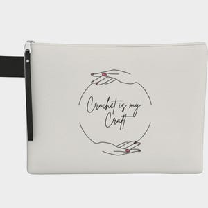 May include: Cream-colored zippered pouch with a black wrist strap. The pouch features the text "Crochet is my Craft" inside a circle formed by two hands with pink nail polish.