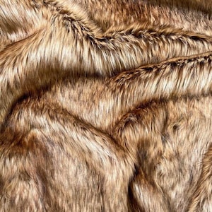 May include: A close-up shot of faux fur fabric. The material has long, flowing fibres in shades of brown, tan, and black, creating a rich, textured appearance. The fabric is densely packed, with visible waves and folds.